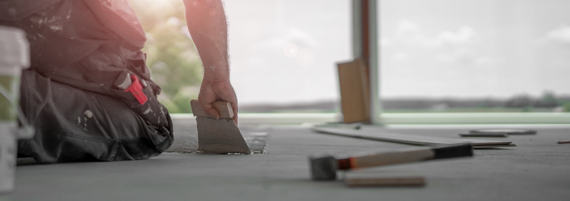 Handwerker verteilt den parkettkleber mit der kleberspachtel auf dem frischen estrich beim parkett legen jpg