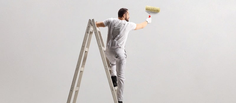 Rear view of a painter painting a wall on a ladder