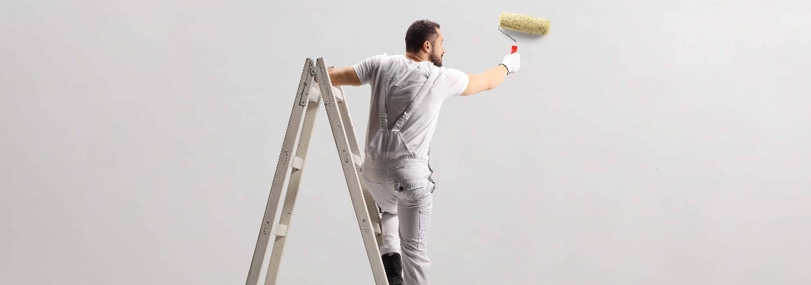 Rear view of a painter painting a wall on a ladder
